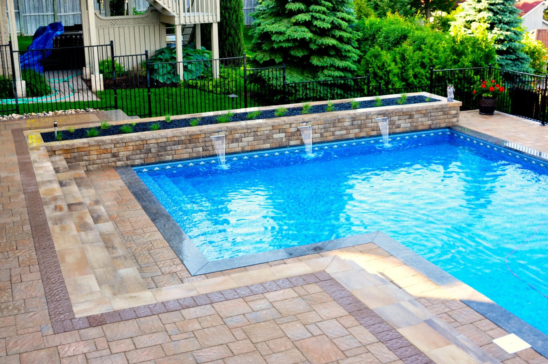 A pristine backyard pool with clear water, surrounded by stone tiles and lush green plants, creating a serene, inviting outdoor setting.