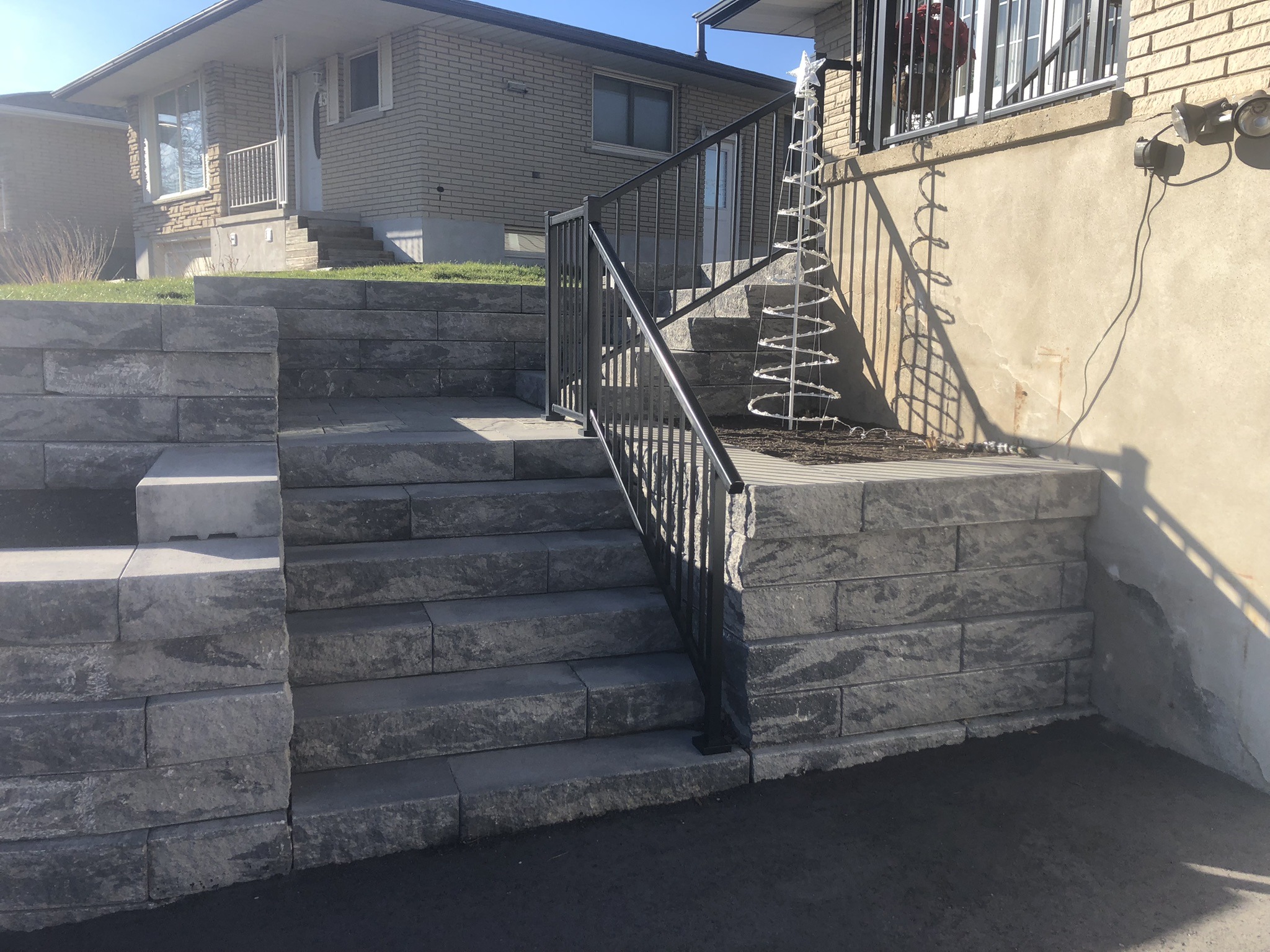 Concrete steps lead to a house with decorative metal railings and a wire-frame display, under a clear blue sky.