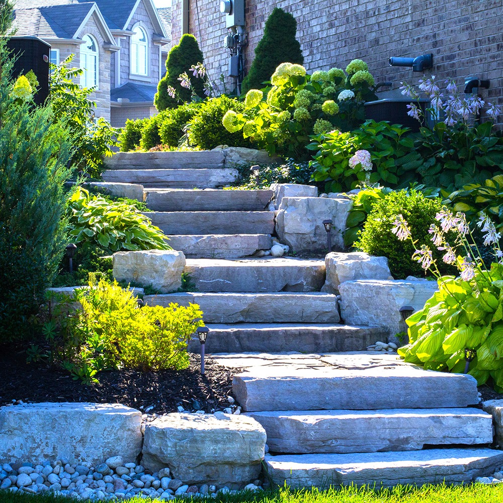 Stone steps adorned with lush greenery and blooming flowers lead to a charming brick house, set in a tranquil garden.