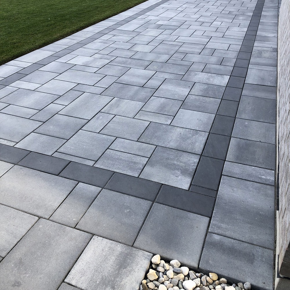 A neatly arranged modern patio with gray pavers, a strip of decorative stones, and a small patch of grass on the side.