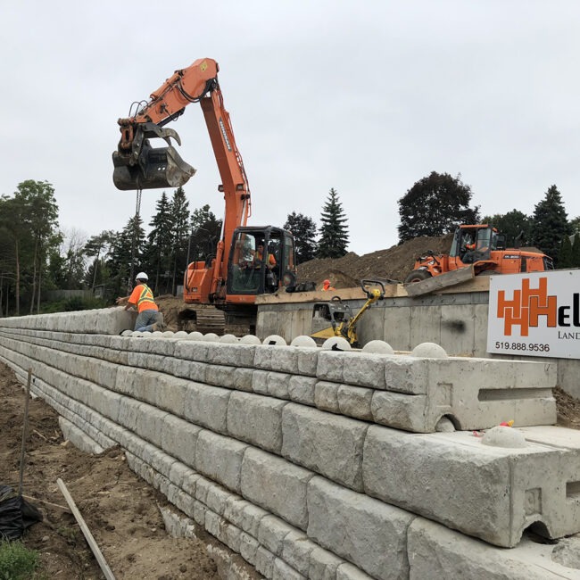 The Helmutz team building a stone retaining wall with a crane and other equipment.