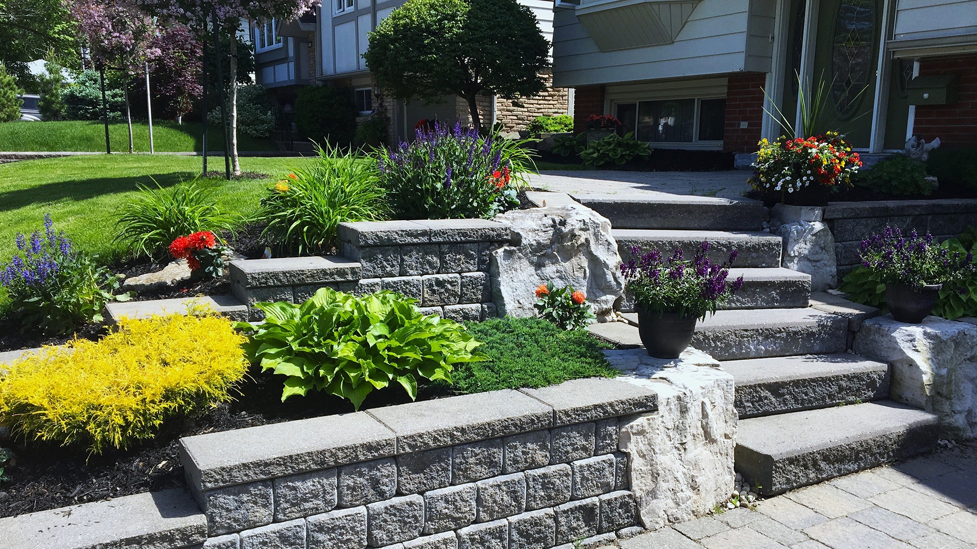 A beautifully landscaped garden with stone steps, colorful flowers, and lush greenery leading to a house, creating a serene and inviting entrance.