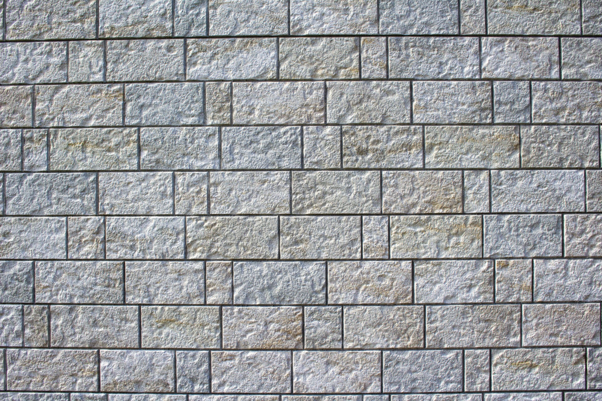 Textured stone wall with evenly arranged rectangular blocks, showcasing various shades of gray and subtle imperfections, creating a visually engaging pattern.