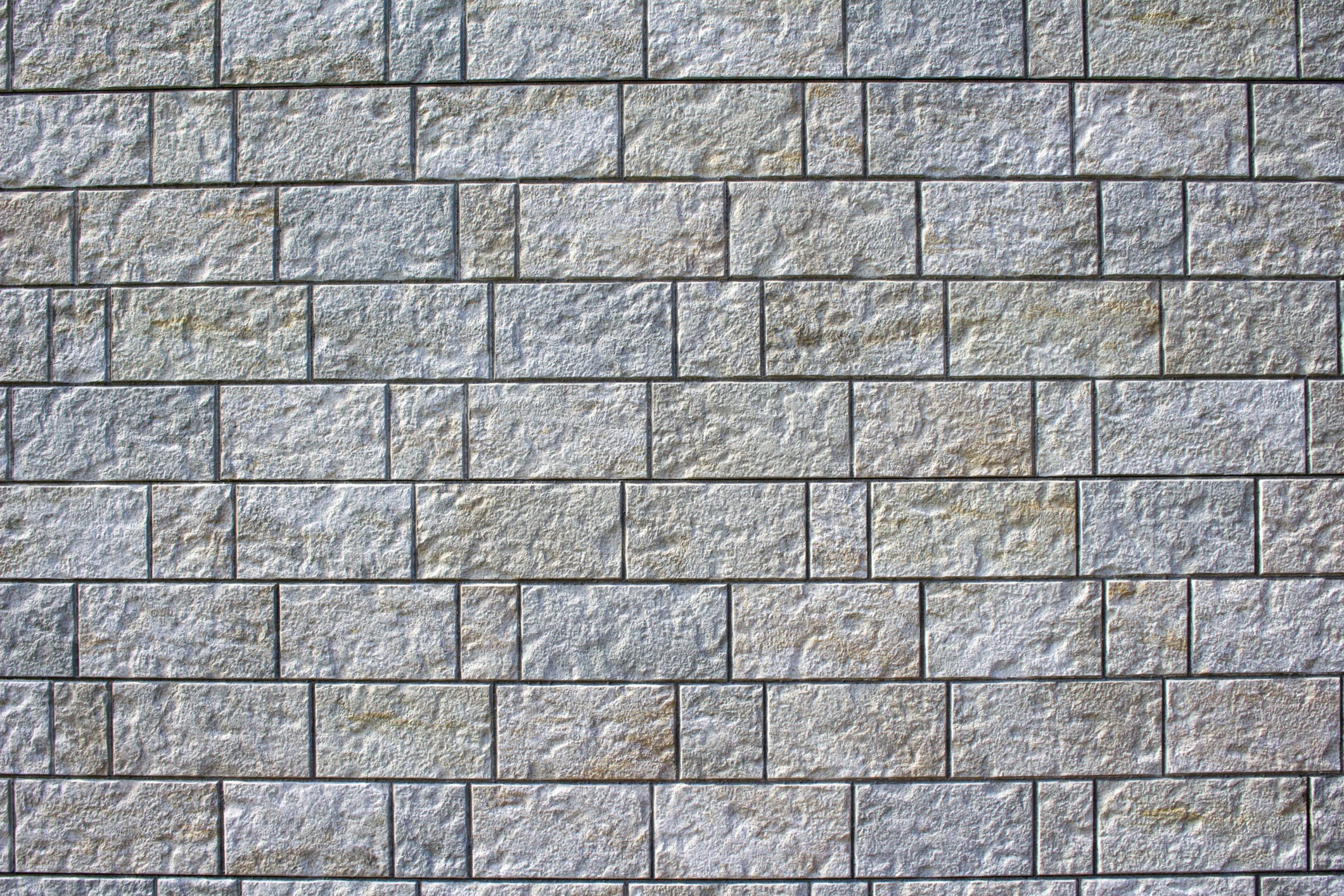 Textured stone wall with evenly arranged rectangular blocks, showcasing various shades of gray and subtle imperfections, creating a visually engaging pattern.