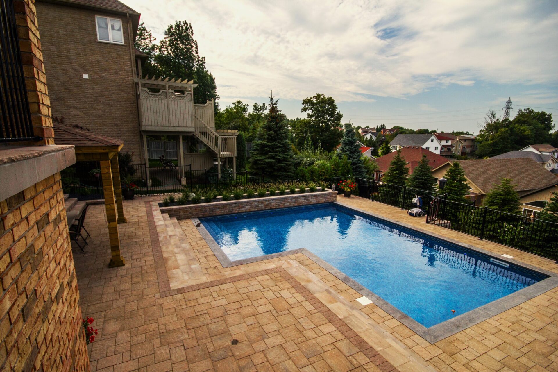 Backyard with rectangular swimming pool, stone patio, and landscaped greenery.