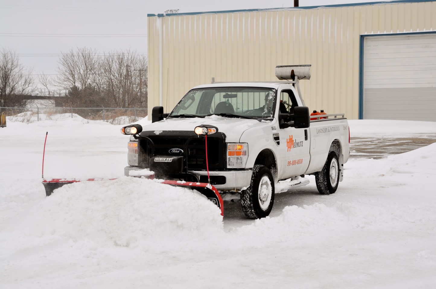 White pickup truck with plow pushing snow in lot