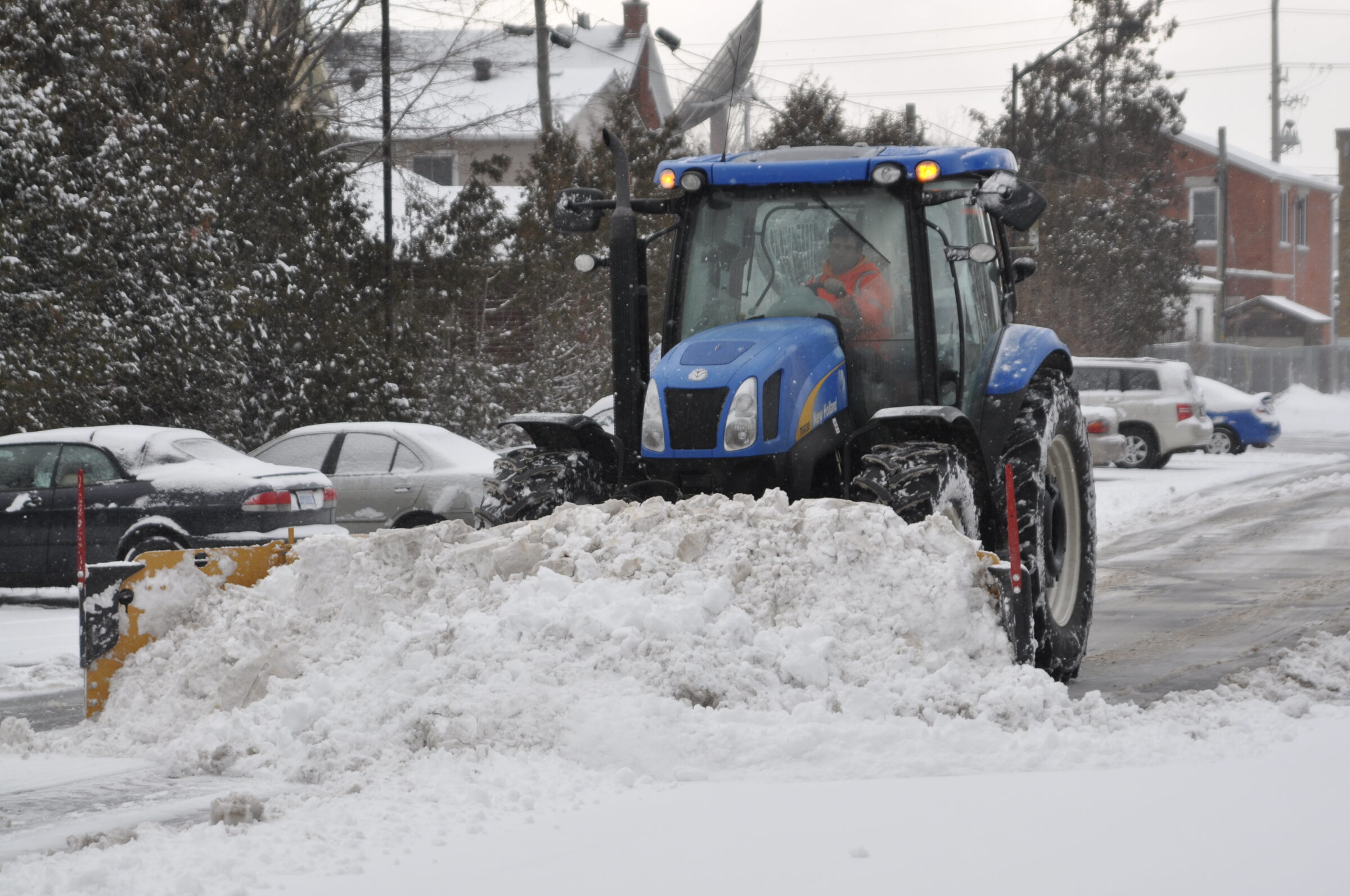 Blue tractor plowing heavy snow on a street