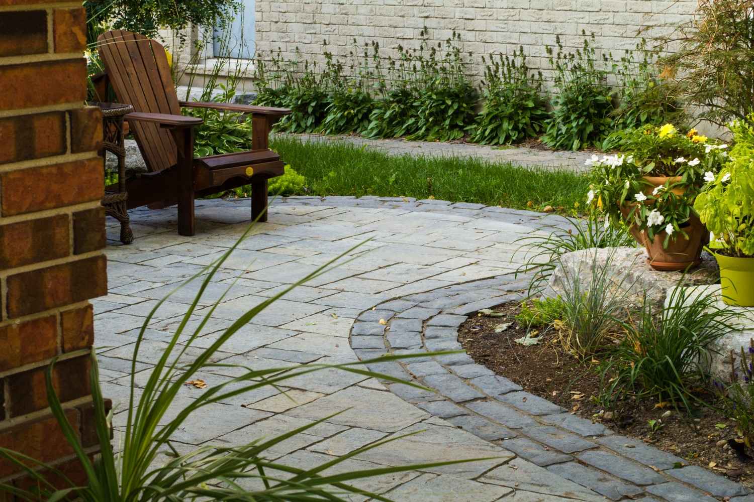 Stone patio with wooden chair, potted plants, and garden greenery.
