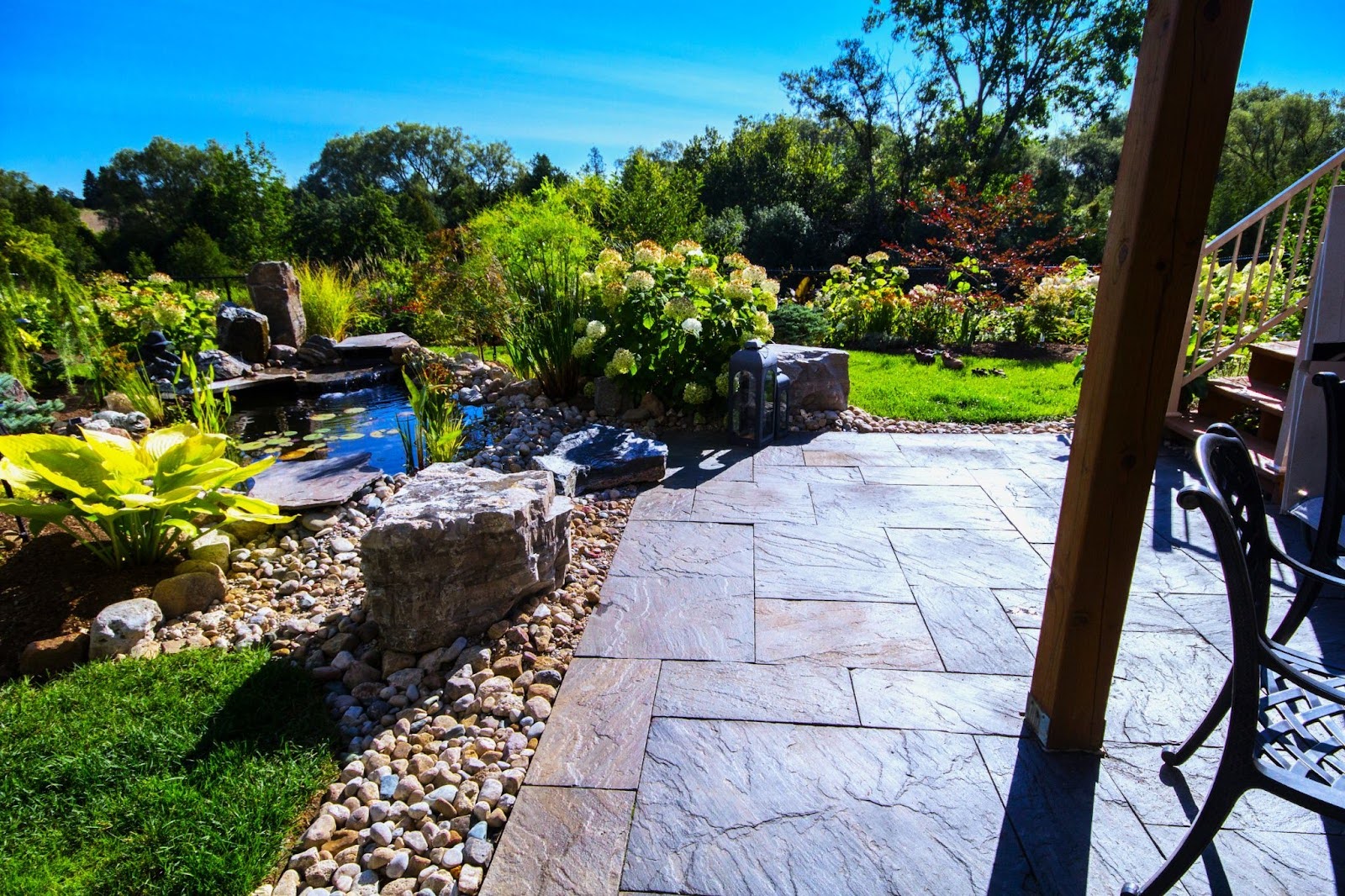 Patio beside pond with stone edging and lush plants.