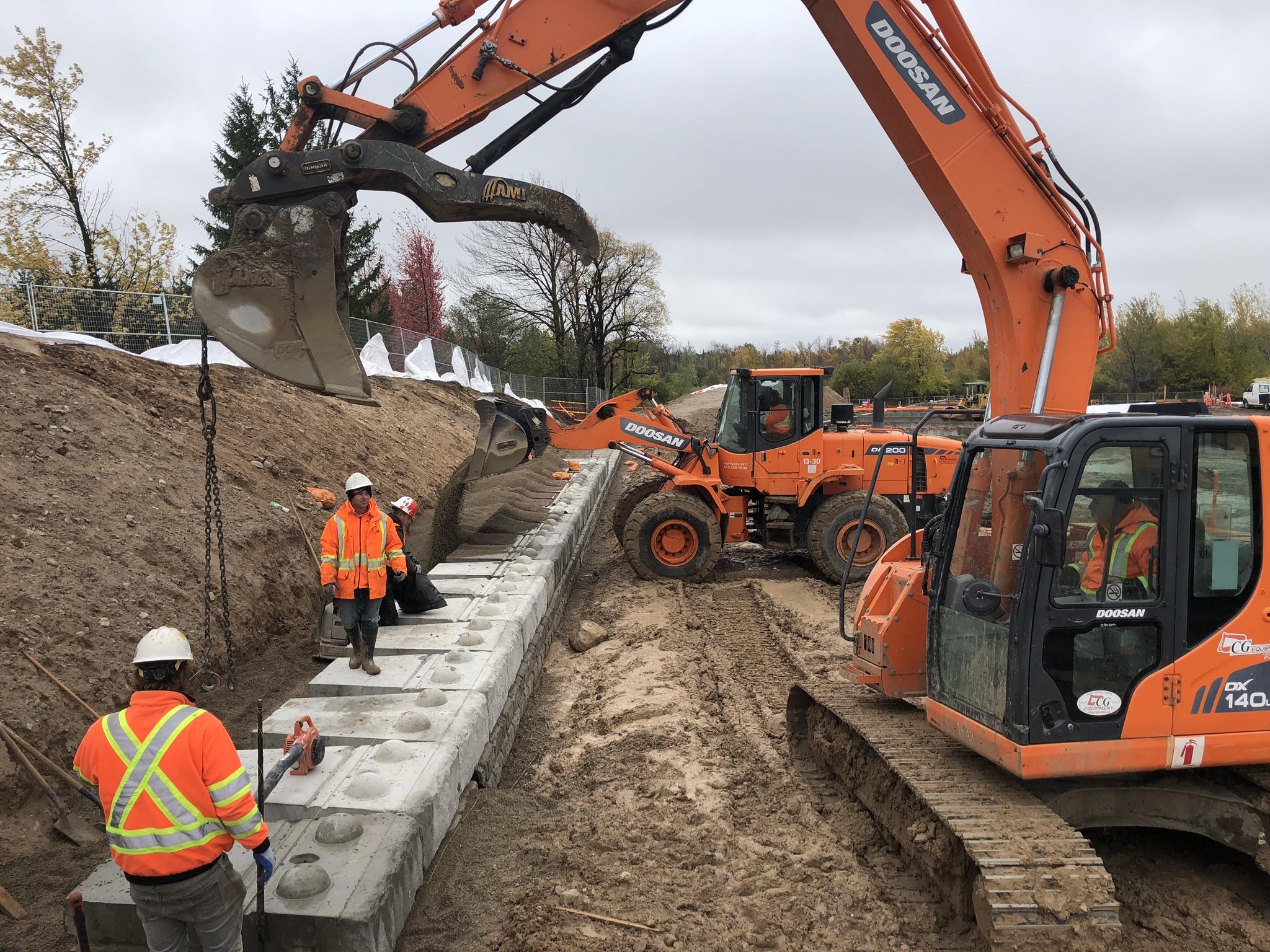 Excavator installing large retaining wall blocks