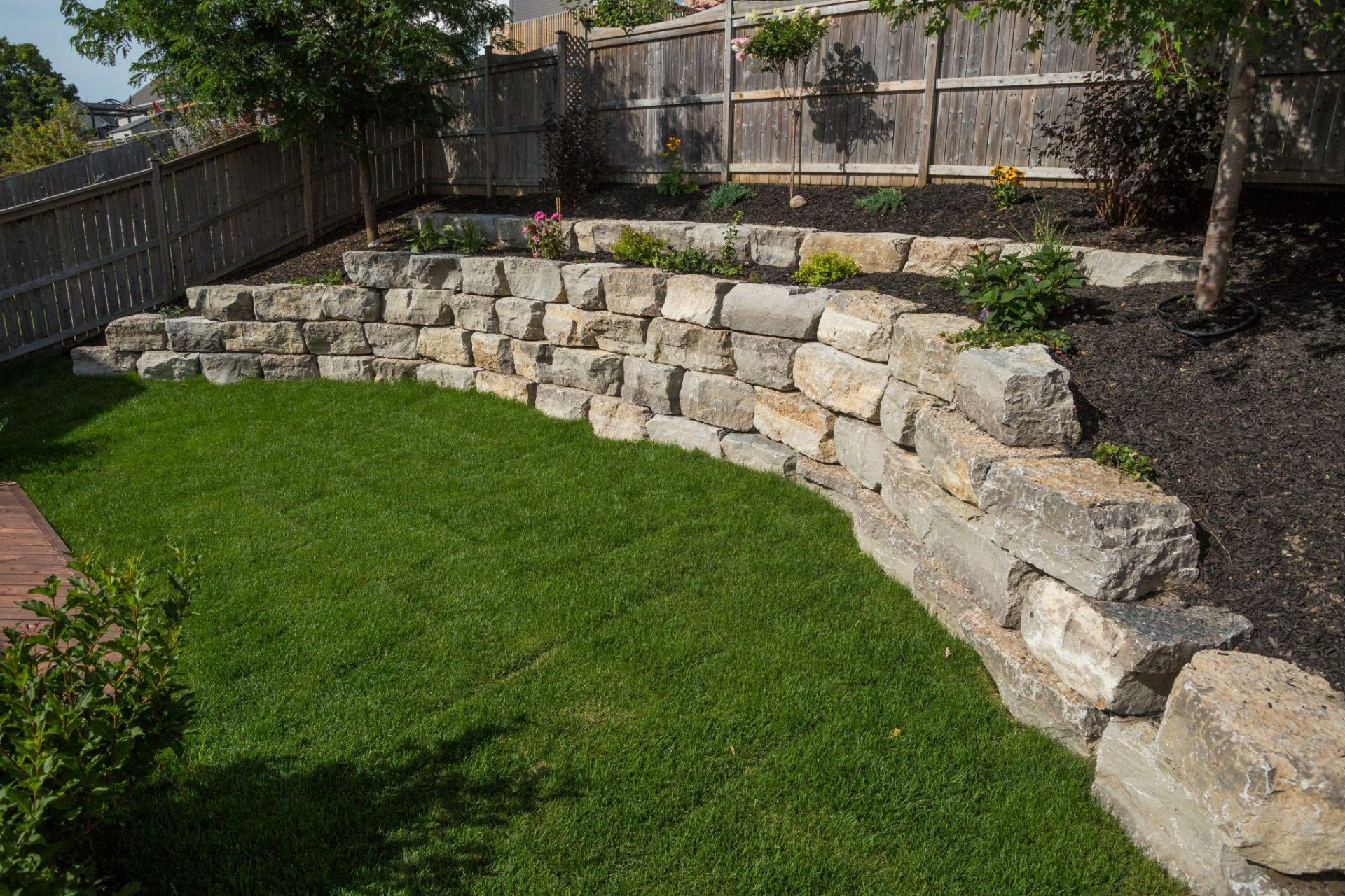 Multi level natural stone retaining wall with planting beds overlooking a manicured lawn.