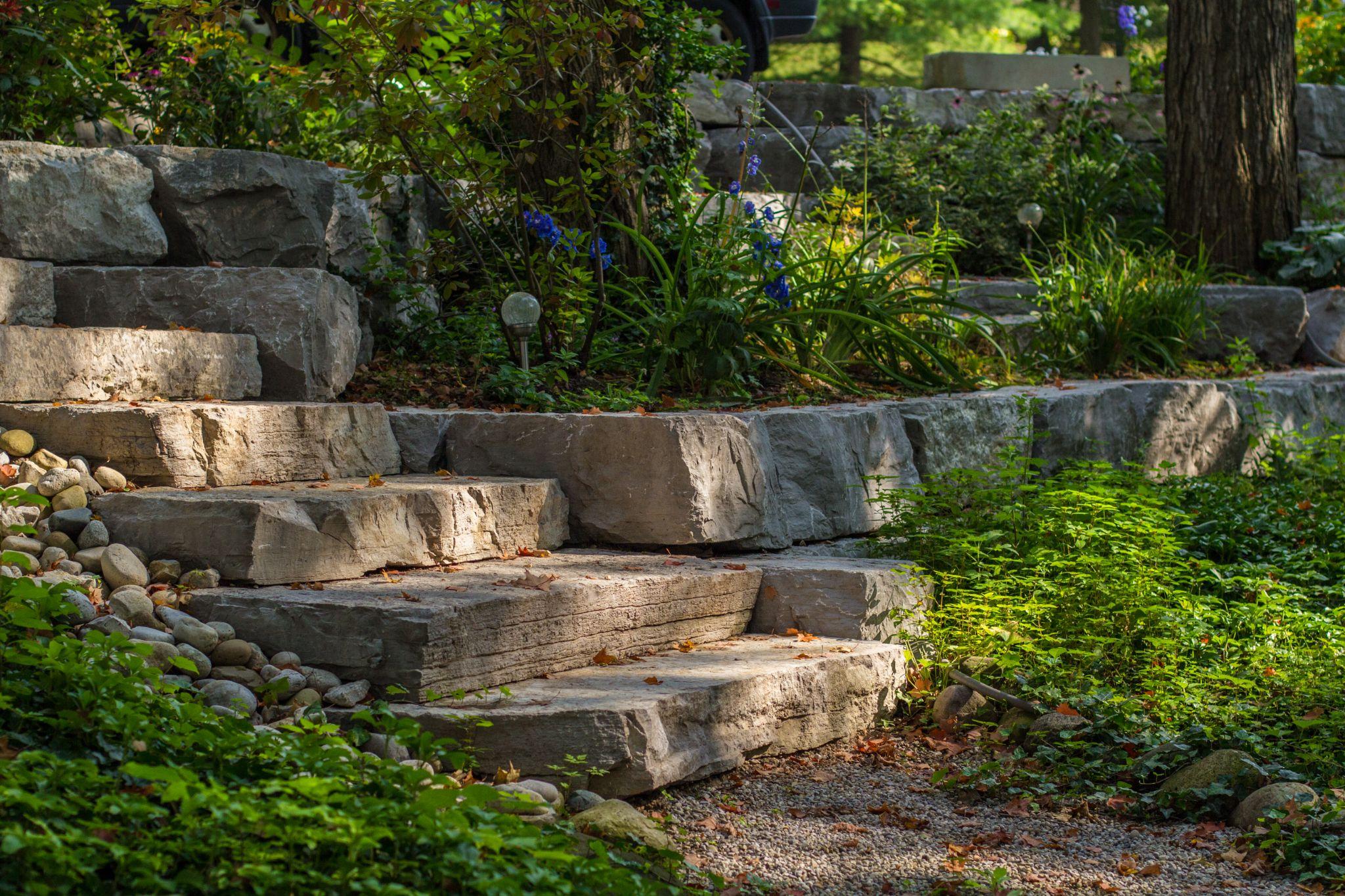 Natural stone landscape steps built into a garden hillside with layered armour stone and lush planting.