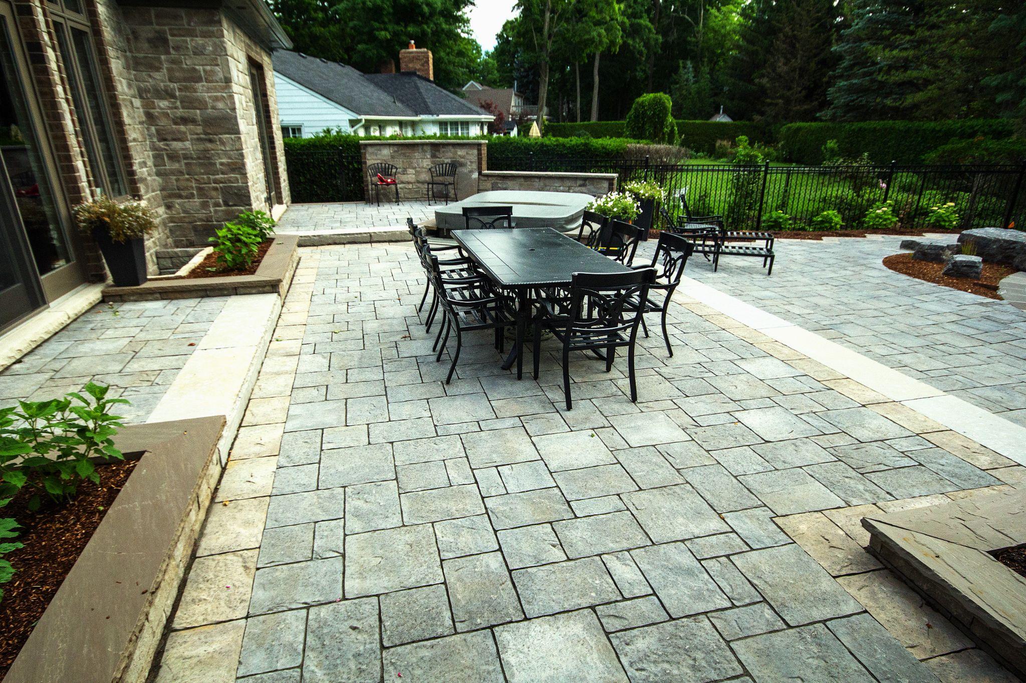 Spacious backyard patio with large format interlocking pavers, dining area, and raised stone step transitions.