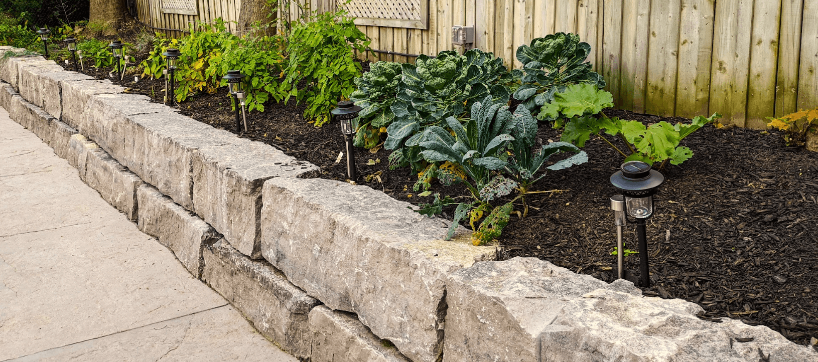 A high-quality stone retaining wall with garden beds on top, green plants growing out of them.