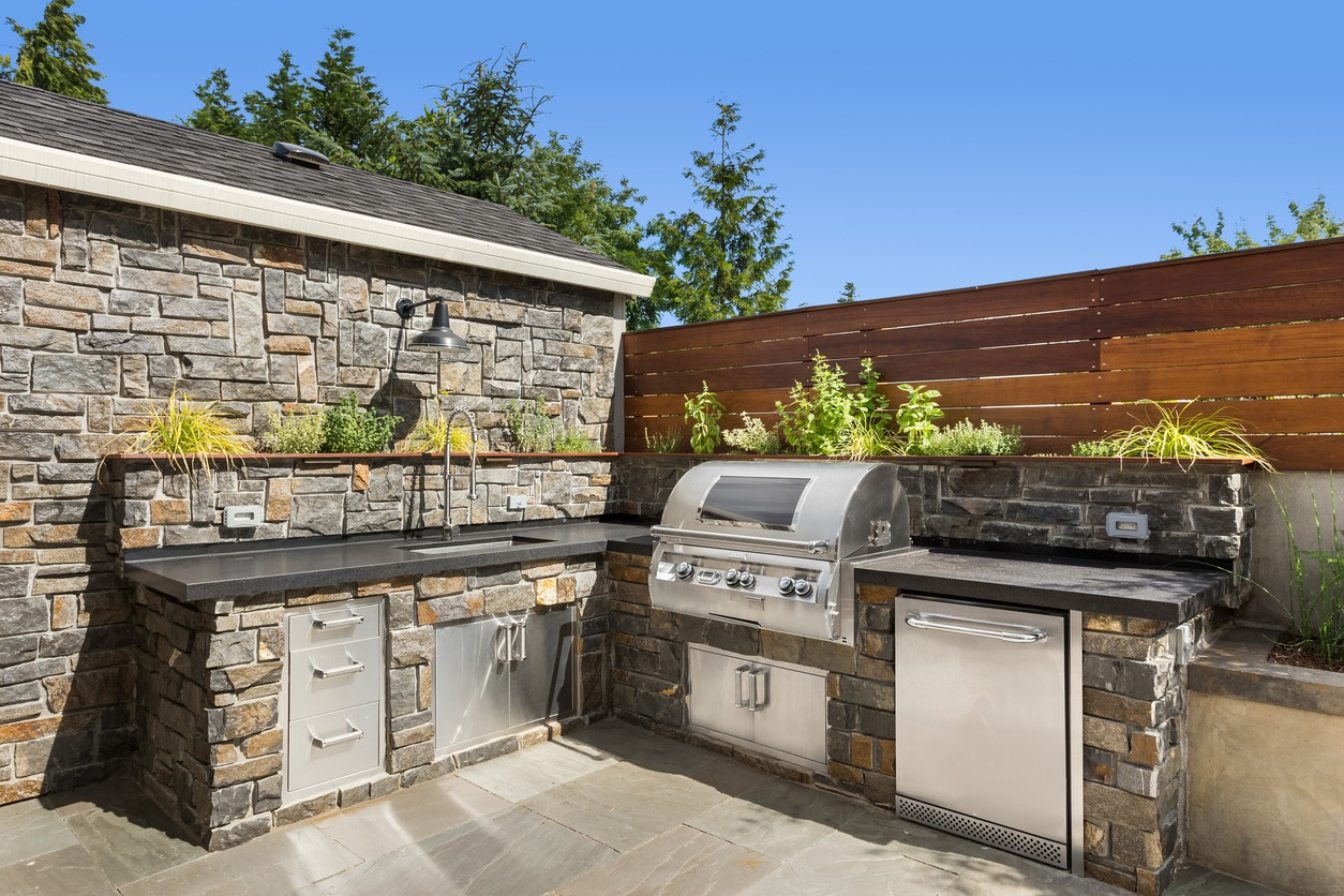 An outdoor kitchen featuring detailed stone masonry work and modern stainless steel appliances
